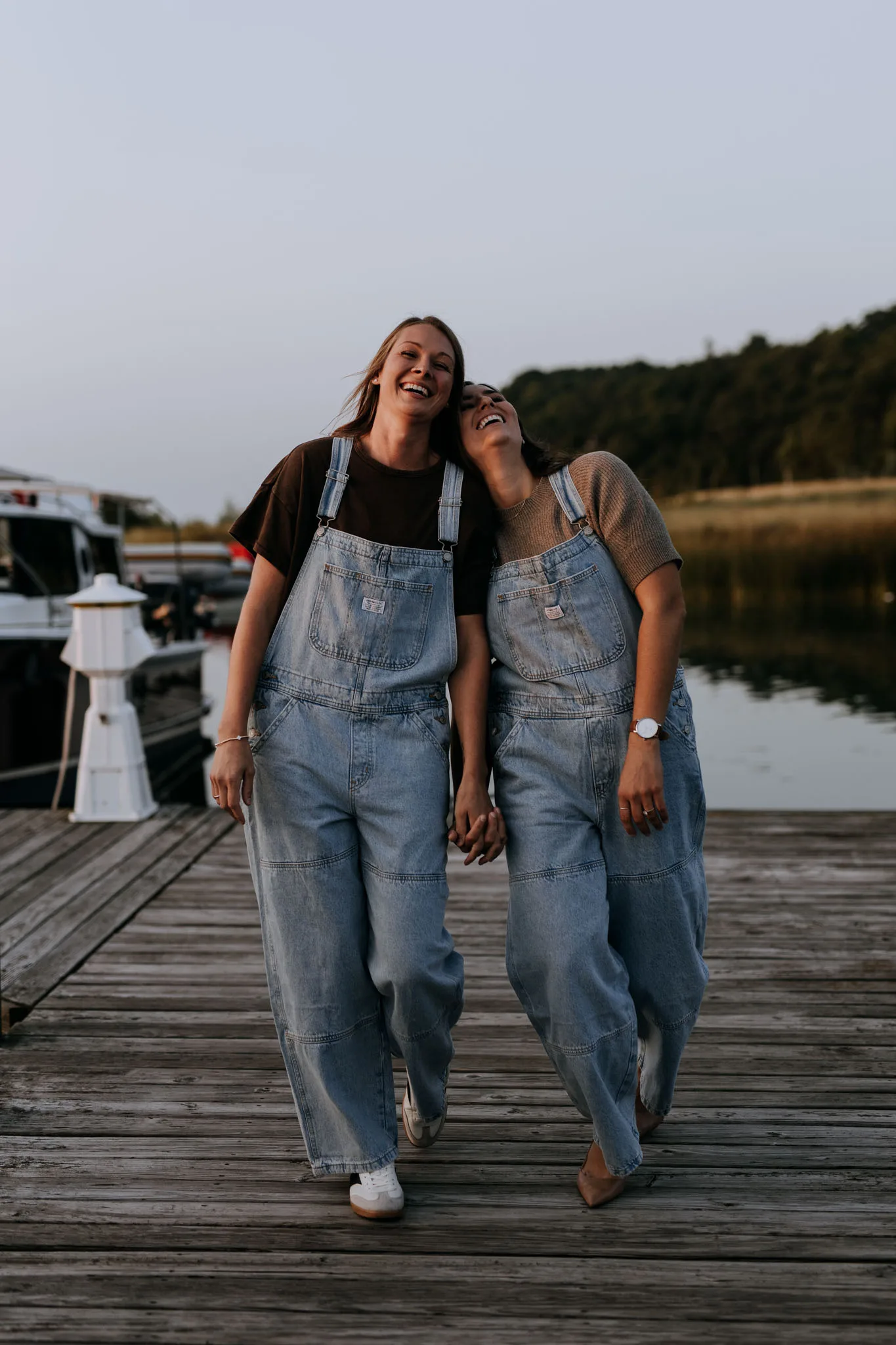 McKenzie and Kayla walking the dock at Leland Marina hand in hand, both in denim overalls