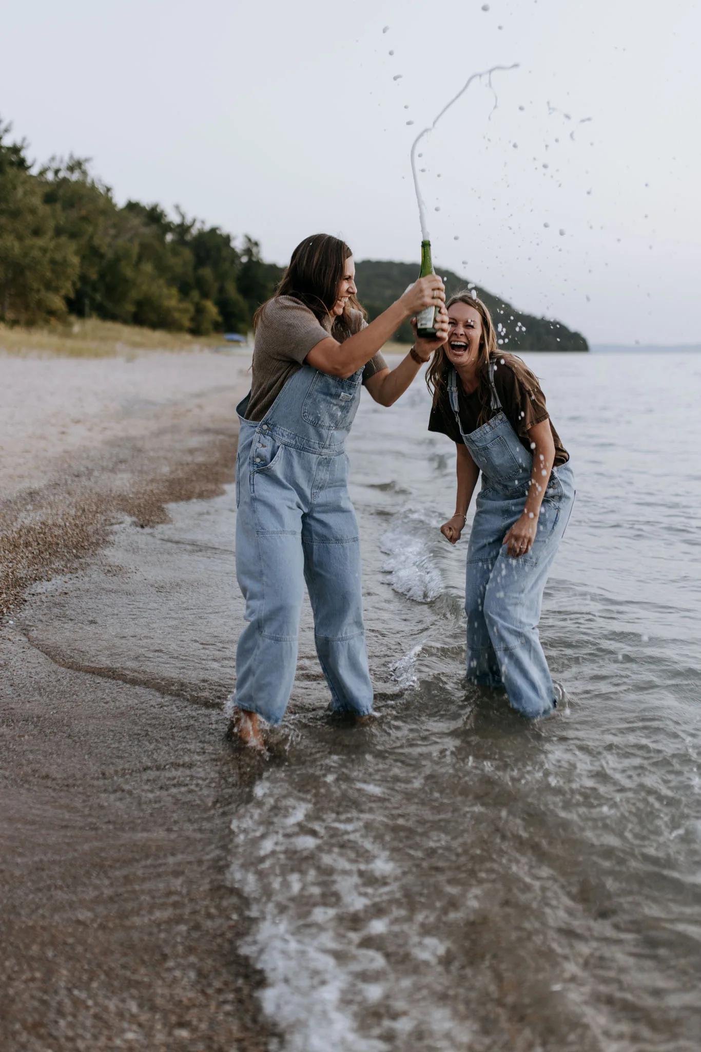 McKenzie and Kayla spraying a bottle of sparkling wine while standing in the water at Van's Beach