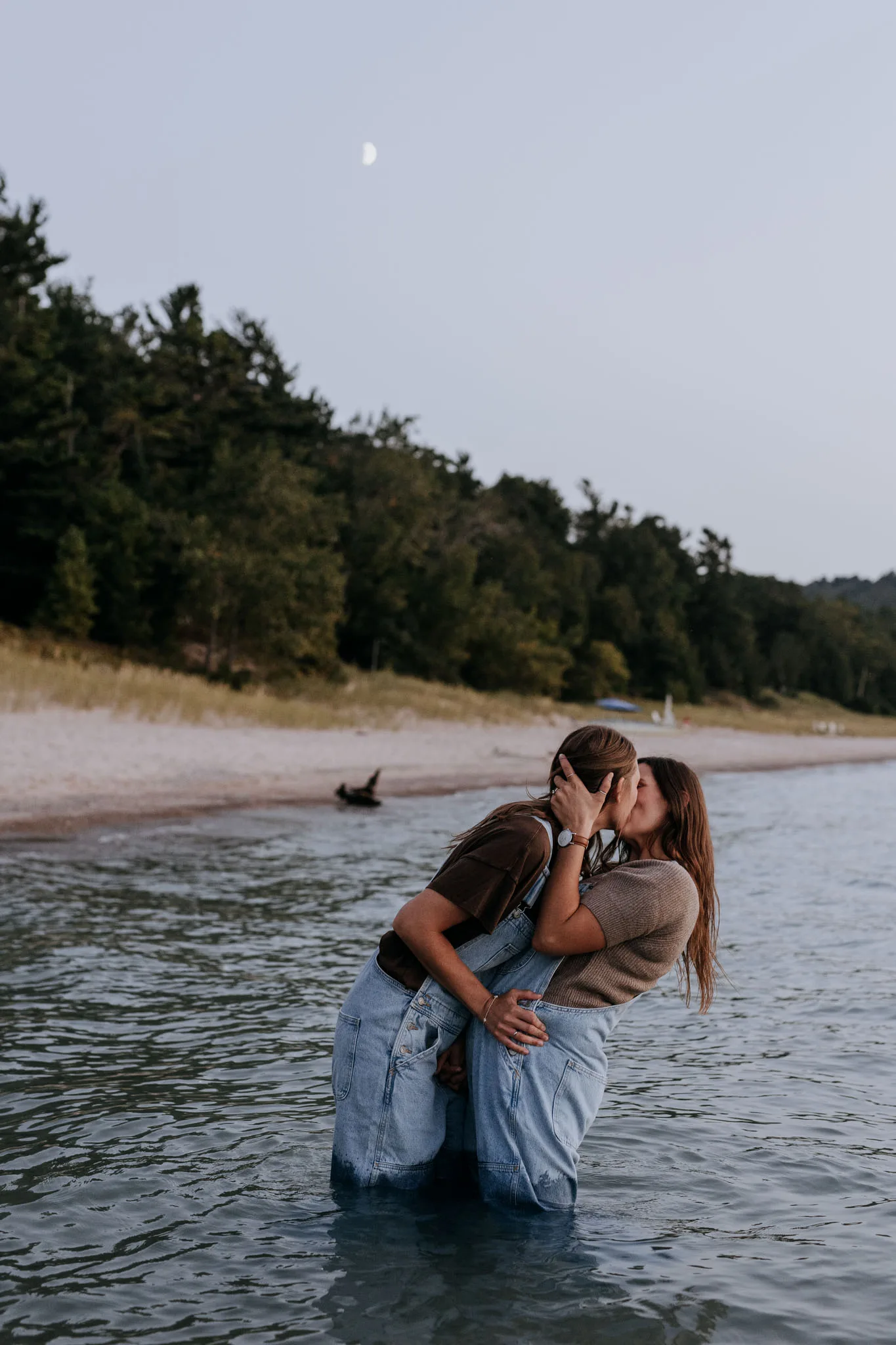 McKenzie and Kayla holding each other waist deep in the water at Van's Beach with the moon above the shore behind them