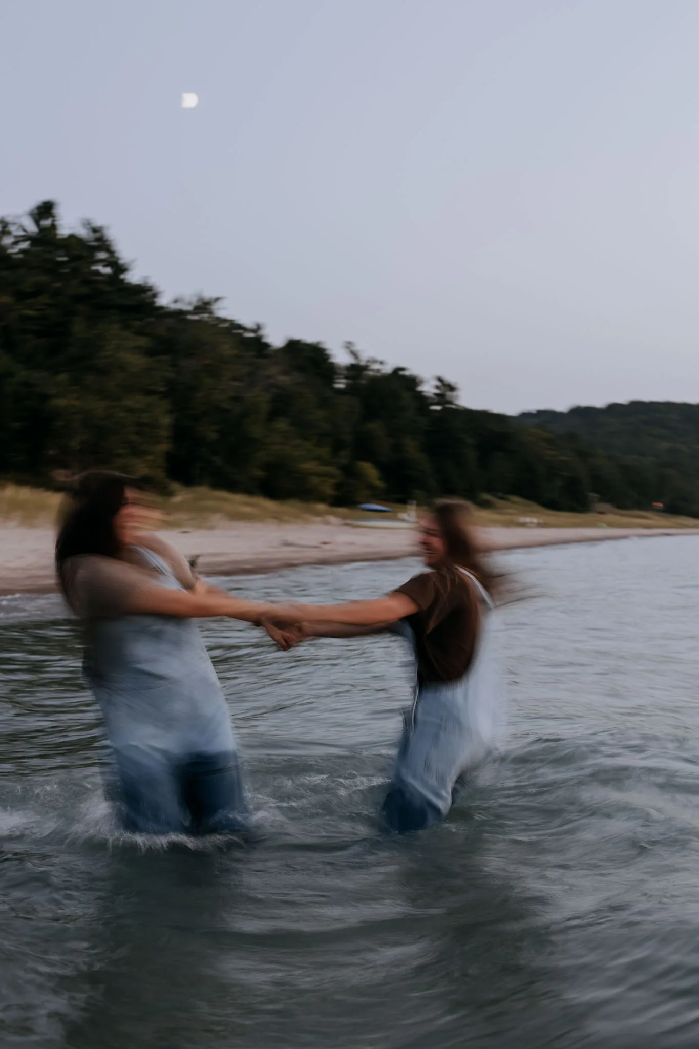 McKenzie and Kayla spinning in the water at Van's Beach in Leland, motion blurred, with the moon out
