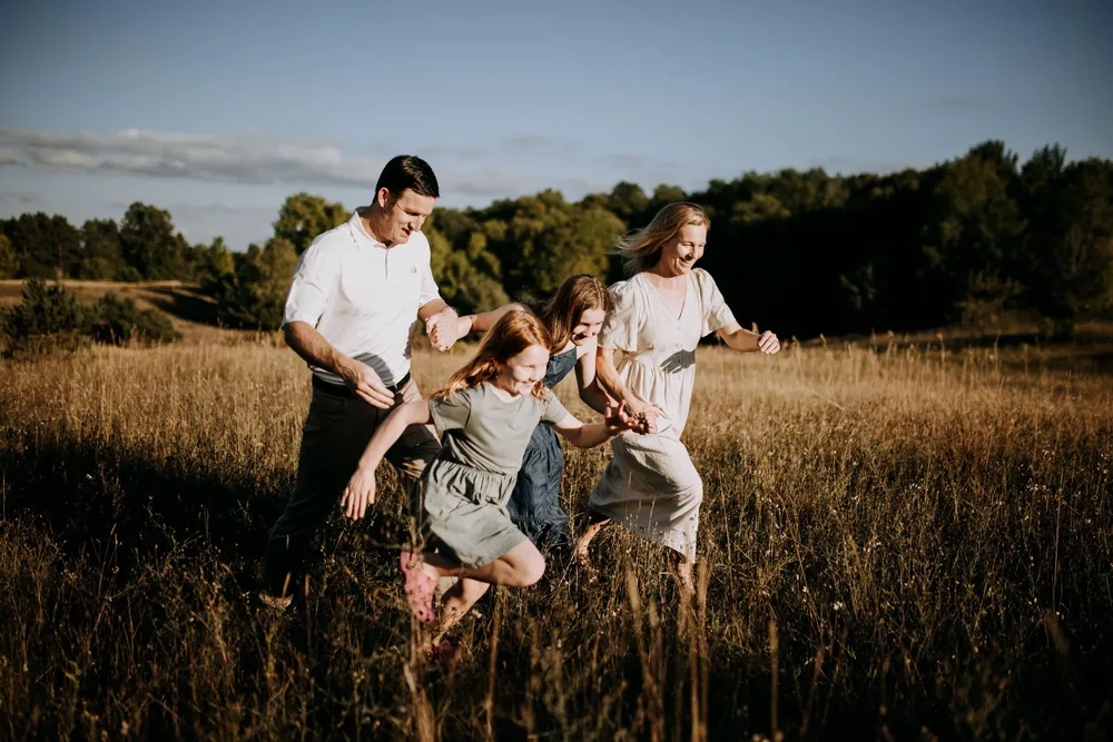 Parents and two kids running through tall grass in a field at sunset