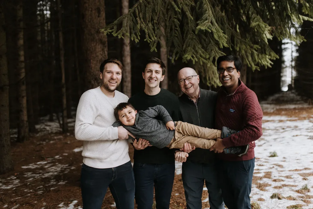 Four men holding a laughing toddler flat between them under the pines