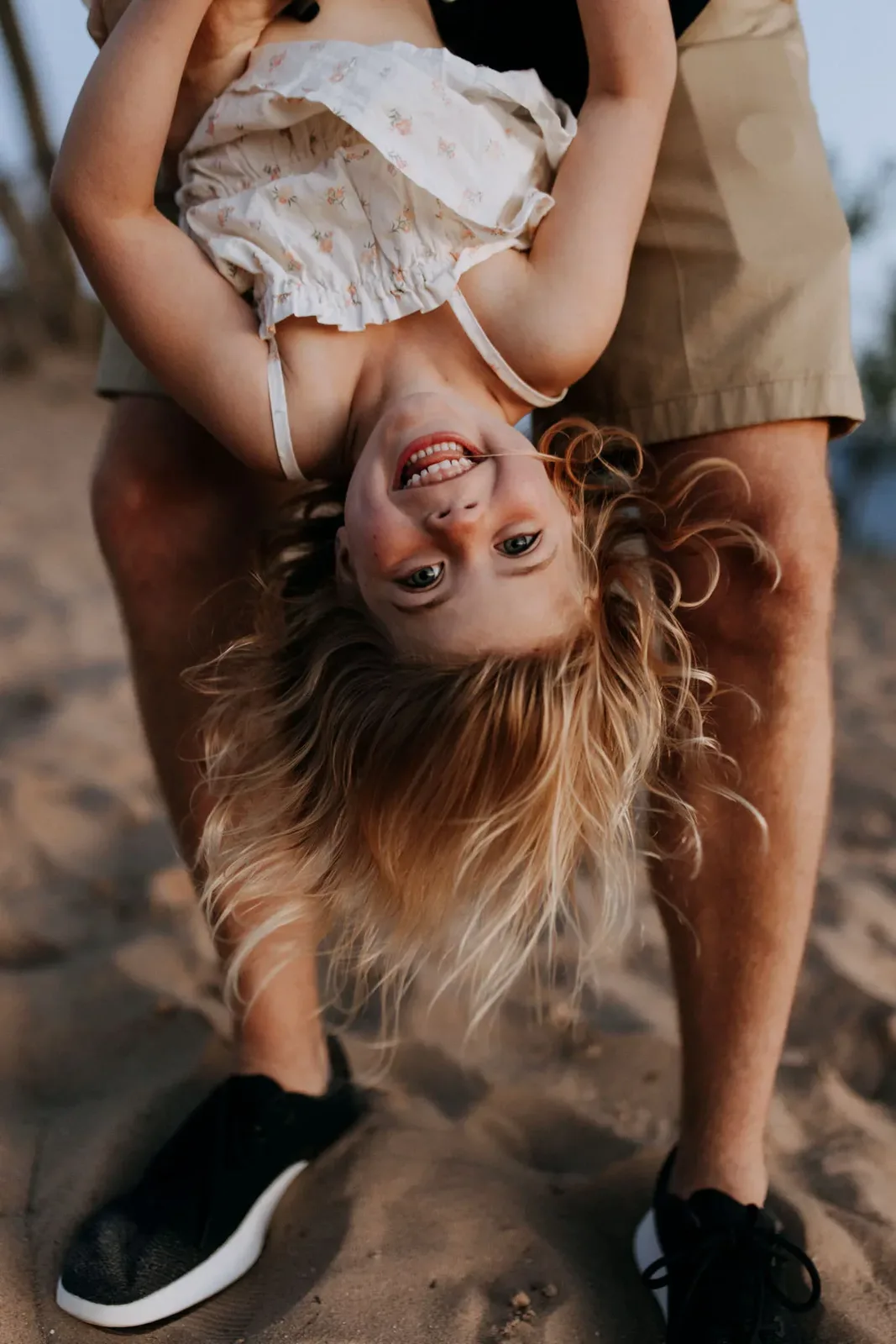 Traverse City family photographer: a little girl held upside down by her dad on the beach, laughing