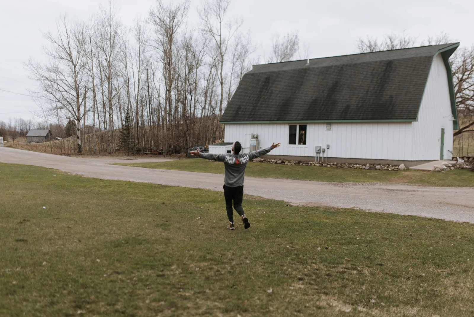 Tiffa running joyfully toward the white barn at Tandem Ciders wearing her custom sweatshirt with Tandem Ciders on the back