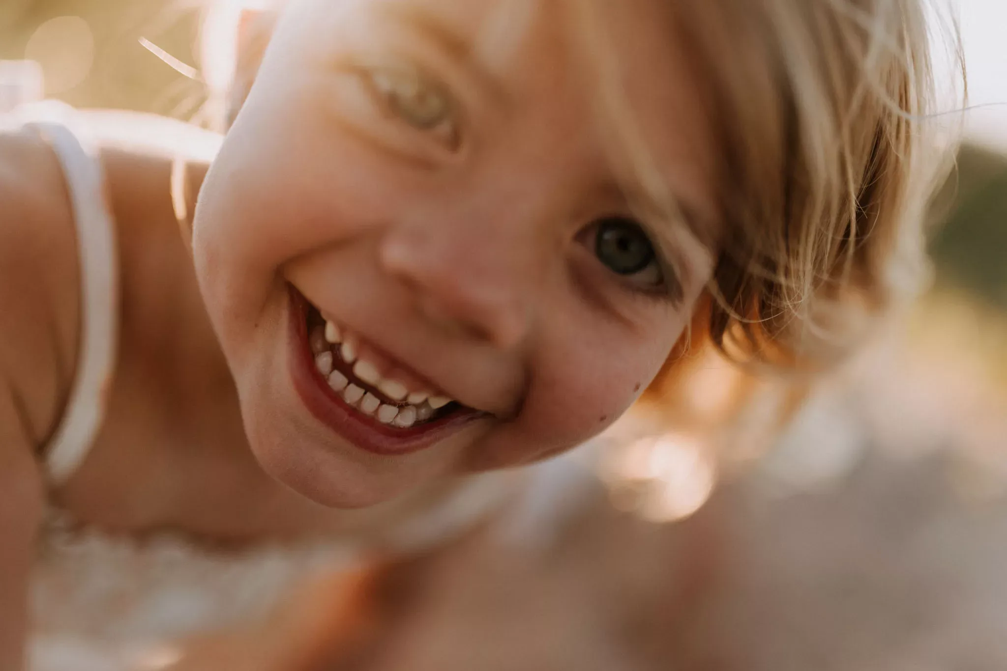 A little girl laughing right into the camera, hair lit gold by the low sun