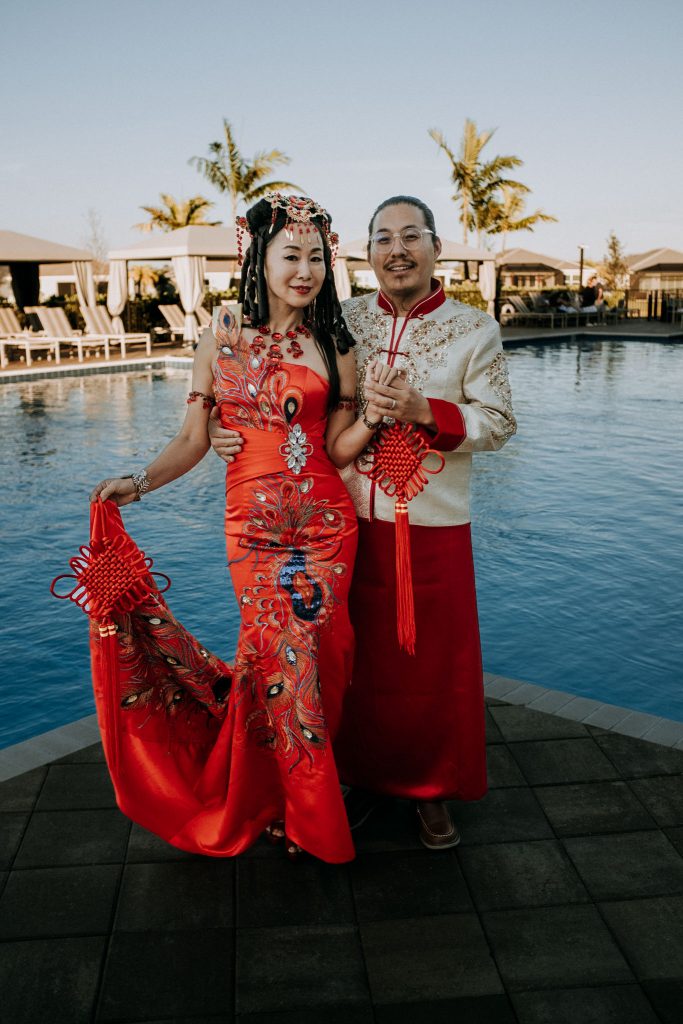 Couple in Traditional Chinese Dress by the pool with palm trees behind