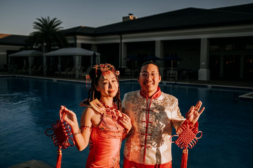 Couple in Traditional Chinese Dress by the pool with palm trees behind