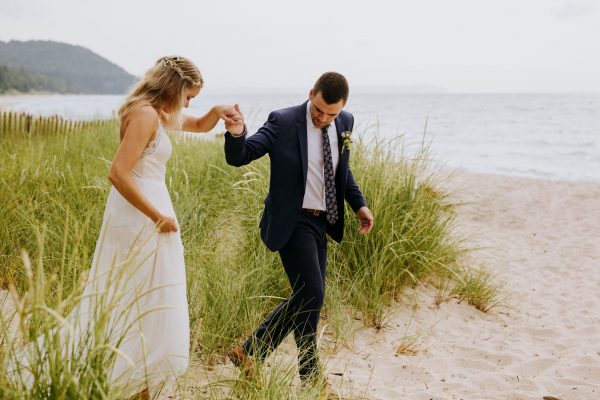 Groom helping bride out of the dune grass on lake michigan